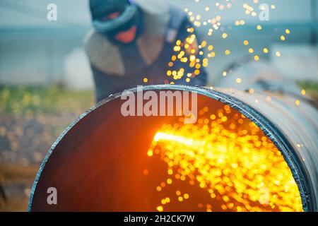 Der Schweißer schneidet große Metallrohre mit Oketylenschweißen. Ein Arbeiter auf der Straße schneidet tagsüber Rohre mit großem Durchmesser und Funken und Feuer fliegen. Stockfoto