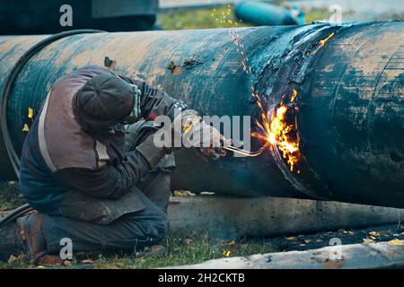 Der Schweißer schneidet große Metallrohre mit Oketylenschweißen. Ein Arbeiter auf der Straße schneidet tagsüber Rohre mit großem Durchmesser und Funken und Feuer fliegen. Stockfoto