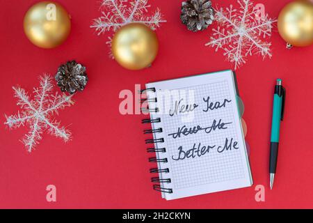 Flacher Weihnachtshintergrund. Notizbuch mit den Worten New year - New me - better me auf rotem Hintergrund mit goldenen Weihnachtskugeln Schneeflocken und Kegeln. Draufsicht Stockfoto