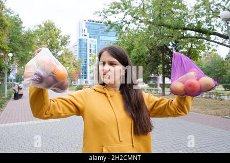 Die Frau hält Gemüse und Obst in einer Plastiktüte und einem Stoffkäufer. Stockfoto