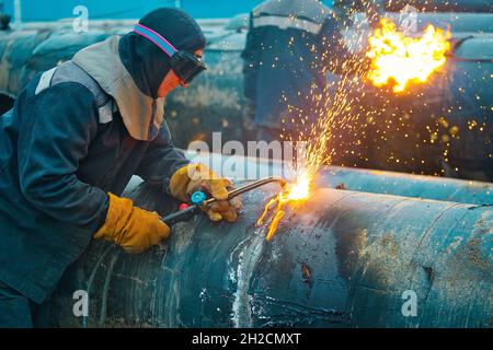 Svrschtschiki Schnitt mit dem Acetylenschweißen die alten Rohre der Gaspipeline des großen Durchmessers. Verwendung von Metallrohren zur Vergasung. Arbeiten Sie tagsüber im Freien. Stockfoto