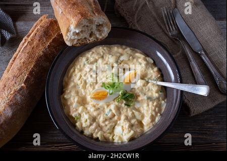 Eiersalat mit frischem Baguette auf einem Holztisch. Traditionelle hausgemachte Gerichte Stockfoto