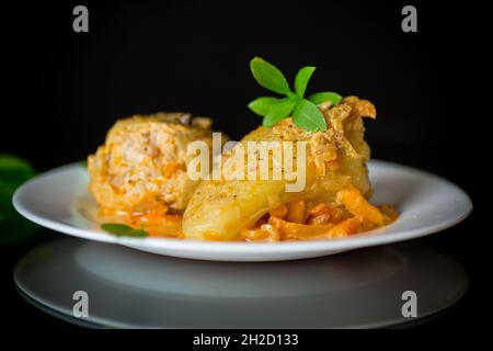 Geschmorte Paprika in Soße, gefüllt mit Fleisch und Reis auf einem Teller auf schwarzem Hintergrund Stockfoto