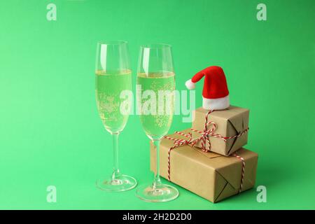 Gläser Champagner, Weihnachtsmütze und Geschenkschachteln auf grünem Hintergrund. Stockfoto