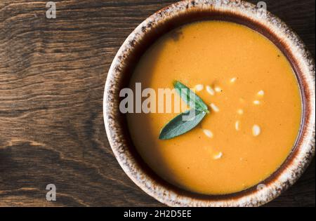 Squashsuppe in Schüssel auf Holztisch mit Salbei und Nussschale Stockfoto