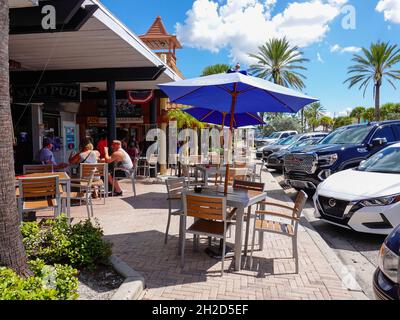Tische mit Sonnenschirmen, Leute, die draußen im John’s Pass Village, Madeira Beach, Florida, USA essen und trinken. Stockfoto