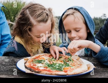 Mädchen und Jungen teilen sich gemeinsam eine Pizza in einem Restaurant im Freien Stockfoto