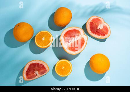 Zitrusfrüchte, Orangen, Grapefruit und der Schatten der Palmblätter auf blauem Hintergrund. Draufsicht, flach liegend. Stockfoto