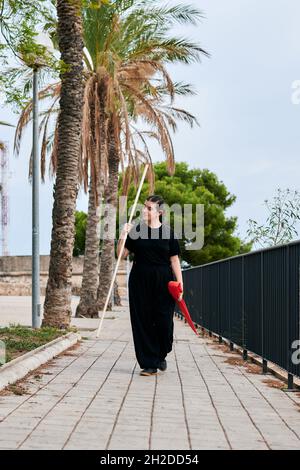 Junge Frau, die nach dem Kung-Fu-Training mit einem Stock im Park spaziert hat Stockfoto