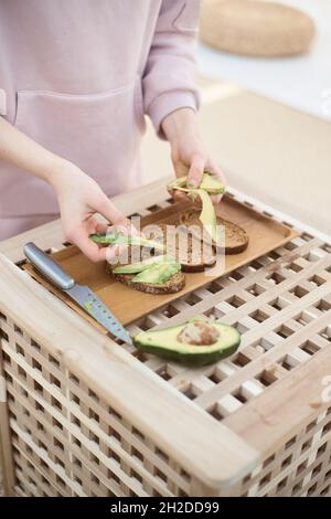 Ein breiter Winkel junger Frau legt Avocado-Scheiben auf Brot Stockfoto