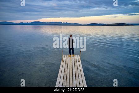 Rückansicht eines nicht erkennbaren Mannes, der auf einem hölzernen Kai in der Nähe des Teiches stand und den Abend in Island genoss Stockfoto