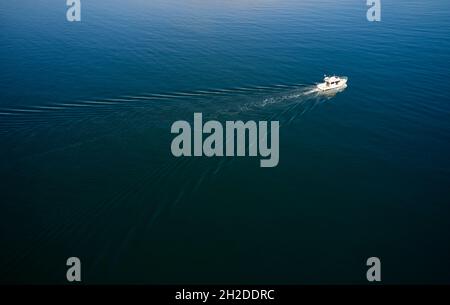 Von oben aus haben Sie einen Blick auf das moderne Motorboot, das bei Tageslicht in Island in ruhiges, azurblaues Meerwasser segelt Stockfoto
