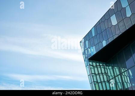 Flache Außenecke eines modernen Gebäudes mit geometrisch geformten Glaspaneelen am wolkenblauen Himmel in Reykjavik in Island Stockfoto