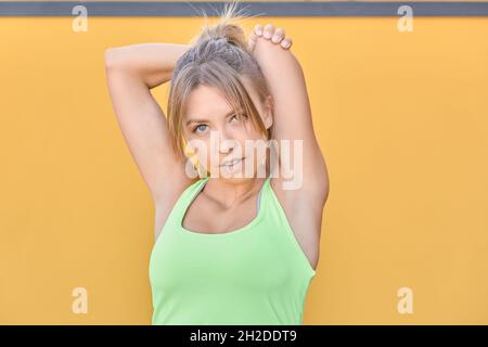 Junges blondes Mädchen mit grünen Augen, das Stretching-Übungen im Garten macht Stockfoto