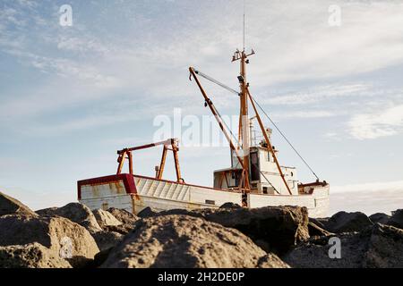 Niedriger Winkel des weißen schäbigen Fischerbootes, der an einem sonnigen Tag in Island an der felsigen Küste festgemacht ist Stockfoto