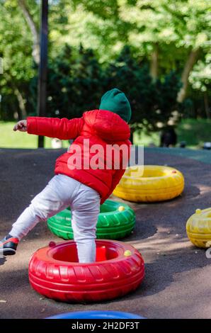 Junge in roter Jacke, der über farbige Reifen springt Stockfoto