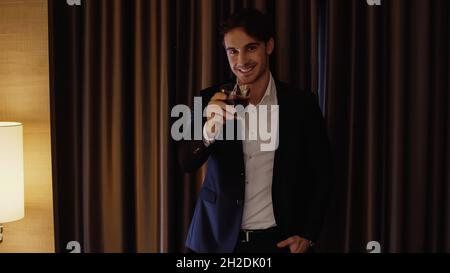 Ein glücklicher Geschäftsmann hält ein Glas Whiskey im Hotelzimmer Stockfoto