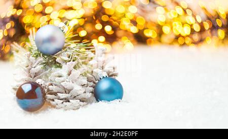 Weihnachtskomposition mit Kegeln im Schnee, blauen Kugeln und Girlande mit Lichtern. Stockfoto