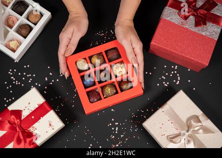 Verschiedene handgemachte Schokoladentrüffel-Bonbons in einer roten Schachtel auf dunklem Hintergrund in weiblichen Händen. Stockfoto