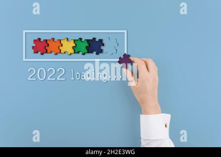 Laden des neuen Jahres 2022 mit man Hand Putting Teil des Puzzles in Fortschrittsbalken. Kreativer Hintergrund für das neue Jahr. Speicherplatz kopieren. Stockfoto