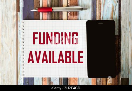 Finanzierung verfügbarer Text auf einem Notizblock mit einem Telefon und einem Stift auf einem gestreiften Hintergrund geschrieben. Sponsor Finanzierung Business Start-up-Projekte Konzept. Stockfoto