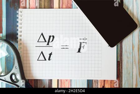Newtons Formel auf einem Notizbuch, in der Nähe einer Lupe und einem Mobiltelefon auf einem gestreiften Hintergrund. Stockfoto