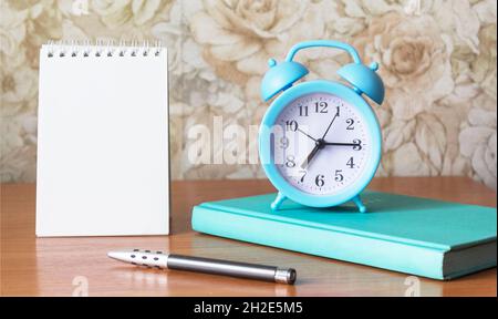 Arbeitsplatz auf einem Holztisch zu Hause. Notizblock zum Schreiben, Tagebuch, Stift und Wecker liegen auf dem Tisch. Stockfoto