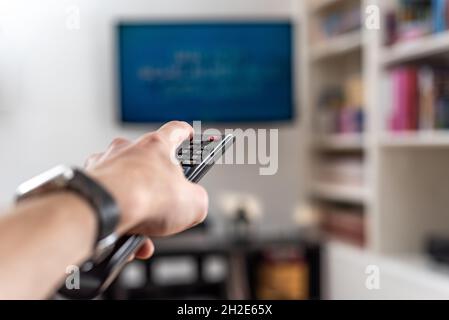 Mann wechselt die Sender auf einem Plasma-Fernseher mit Fernbedienung zu Hause Stockfoto