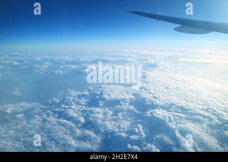 Der Flugzeugflügel am strahlend blauen Himmel und die flauschigen weißen Wolken blicken während des Fluges vom Flugzeugfenster aus Stockfoto