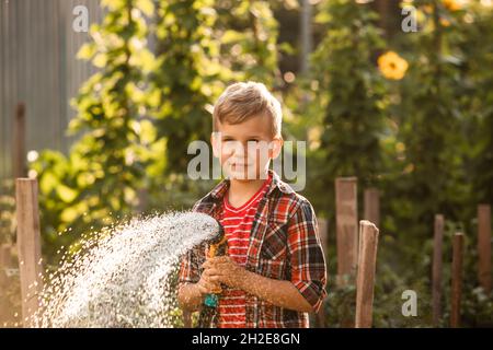 Der kleine Junge wäscht die Pflanzen und macht große Wasserspritzer Stockfoto