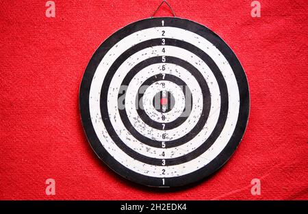 Gebrauchte Dartscheibe, die auf rotem Teppich und seinen Schatten steht. Stockfoto