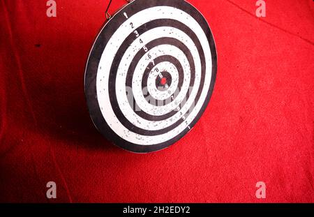 Gebrauchte Dartscheibe, die auf rotem Teppich und seinen Schatten steht. Stockfoto