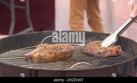 Steak aus nächster Nähe auf dem Grill. Die Nahaufnahme eines unbekannten Köchin dreht auf dem Red-Hot Grill ein Stück köstliches Steak-Friting um. Stockfoto