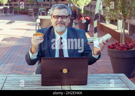 Der Finanzmann hält Geld in den Händen und Bitcoins. Mit seinem Laptop, der an der Börse gehandelt wurde, machte er Geld. Stockfoto