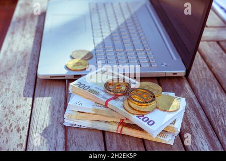 Auf dem Tisch stehen Bitcoins und ein Laptop. Bitcoin-Münzen liegen auf PapierEuro. Stockfoto