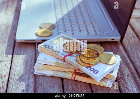 Auf dem Tisch stehen Bitcoins und ein Laptop. Bitcoin-Münzen liegen auf PapierEuro. Stockfoto