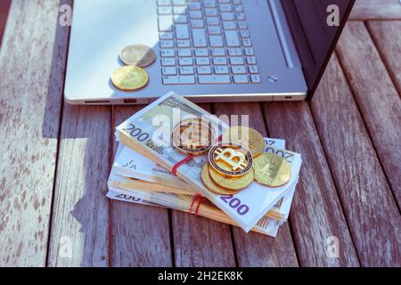 Auf dem Tisch stehen Bitcoins und ein Laptop. Bitcoin-Münzen liegen auf PapierEuro. Stockfoto