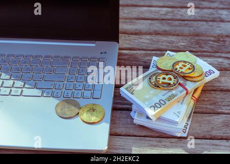 Auf dem Tisch stehen Bitcoins und ein Laptop. Bitcoin-Münzen liegen auf PapierEuro. Stockfoto