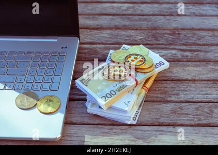 Auf dem Tisch stehen Bitcoins und ein Laptop. Bitcoin-Münzen liegen auf PapierEuro. Stockfoto