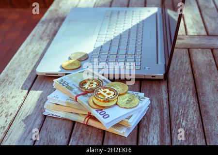 Auf dem Tisch stehen Bitcoins und ein Laptop. Bitcoin-Münzen liegen auf PapierEuro. Stockfoto