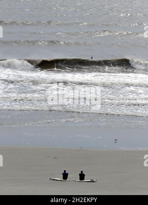 Zwei Surfer sitzen zusammen auf ihren Surfbrettern am Strand und beobachten die Wellen und warten Stockfoto