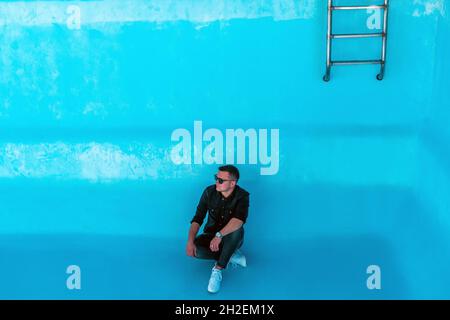 Attraktiver Mann sitzt in leerem Swimmingpool. Stockfoto