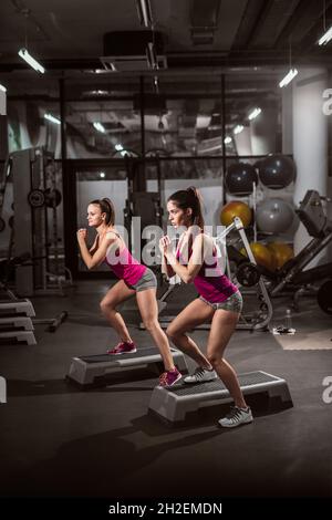 Zwei sportliche Frauen treten im Fitnessstudio auf den Stepper. Gesundes Lifestyle-Konzept. Stockfoto