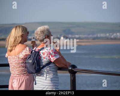 APPLEDORE, DEVON, ENGLAND - 29 2021. AUGUST: Zwei Frauen genießen Eiscreme mit Blick über die Mündung. Sommerabend im Urlaub. Stockfoto