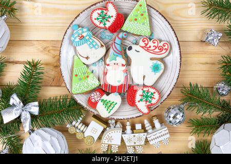 Weihnachts-Lebkuchen, Kekse auf einem natürlichen Holztisch neben Tannenzweigen. Schneeflocke, Schneemann, Hirsch, Weihnachtsmannkekse. Neujahresmodo Stockfoto