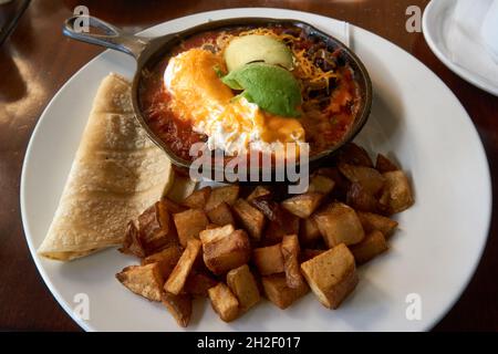 Nahaufnahme eines Tellers mit mexikanischen Huevos Rancheros mit Maistortillas, Avocado und gebratenen Kartoffeln Stockfoto
