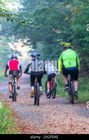 Familien fahren gemeinsam im Wald oder Wald. Erwachsene und Kinder reiten gemeinsam Fahrrad durch einen Waldweg oder einen Waldweg. Familienaktivitäten. Stockfoto