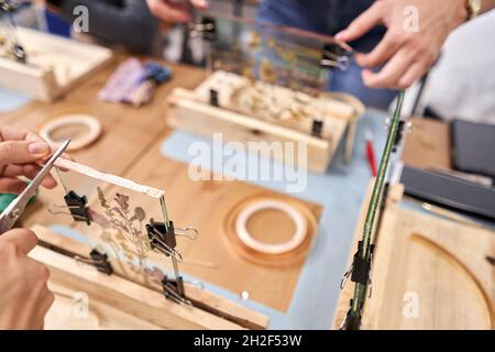 Eine Frau fixiert Glasplatten. Meisterkurs zur Rahmenerstellung mit Herbarium in tiffany-Technik in Buntglas. Herbarium von getrockneten verschiedenen Pflanzen Stockfoto