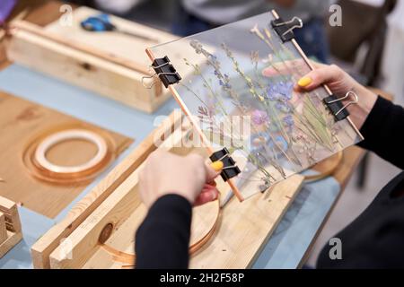 Eine Frau fixiert Glasplatten. Meisterkurs zur Rahmenerstellung mit Herbarium in tiffany-Technik in Buntglas. Herbarium von getrockneten verschiedenen Pflanzen Stockfoto