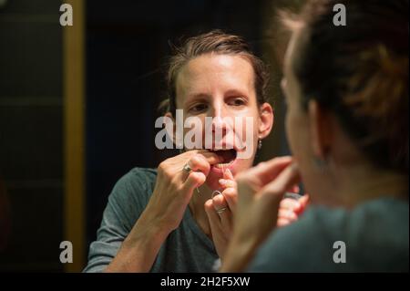Eine junge Frau, die ihre Zähne mit Zahnseide in den Badezimmerspiegel warf. Stockfoto